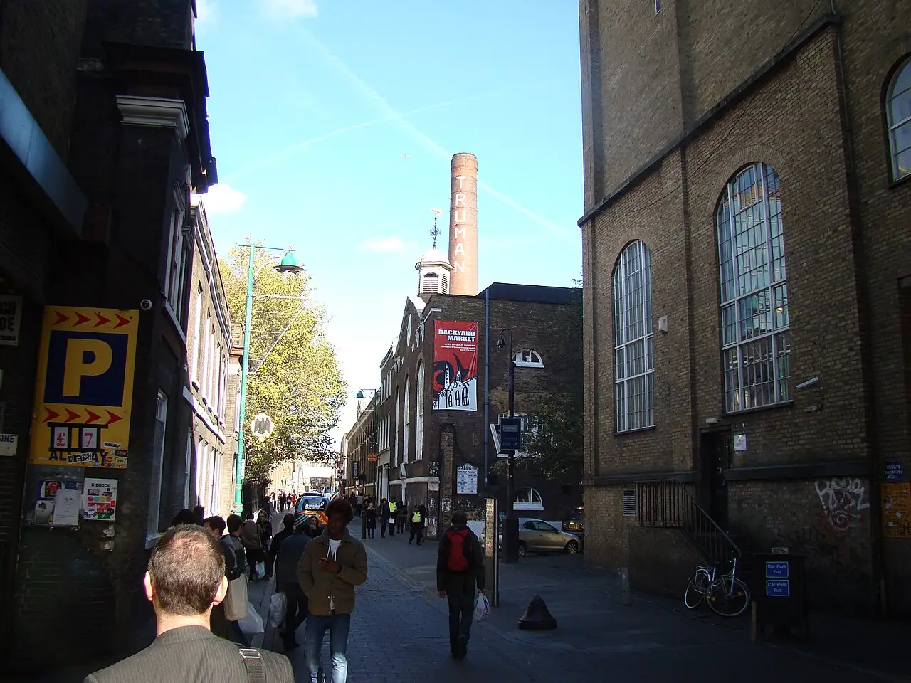 Brick Lane in una giornata di sole: in fondo alla via la ciminiera in mattoni con la scritta Truman sopra l'ex birreria