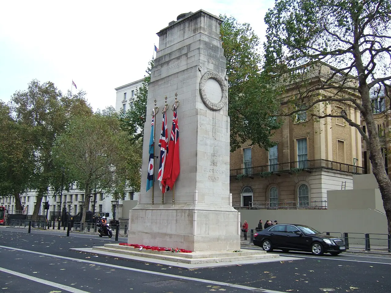 Il Cenotaph su Whitehall: pilone di pietra chiara con tre bandiere sul lato lungo, la scritta «The Glorious Dead» e alberi autunnali intorno