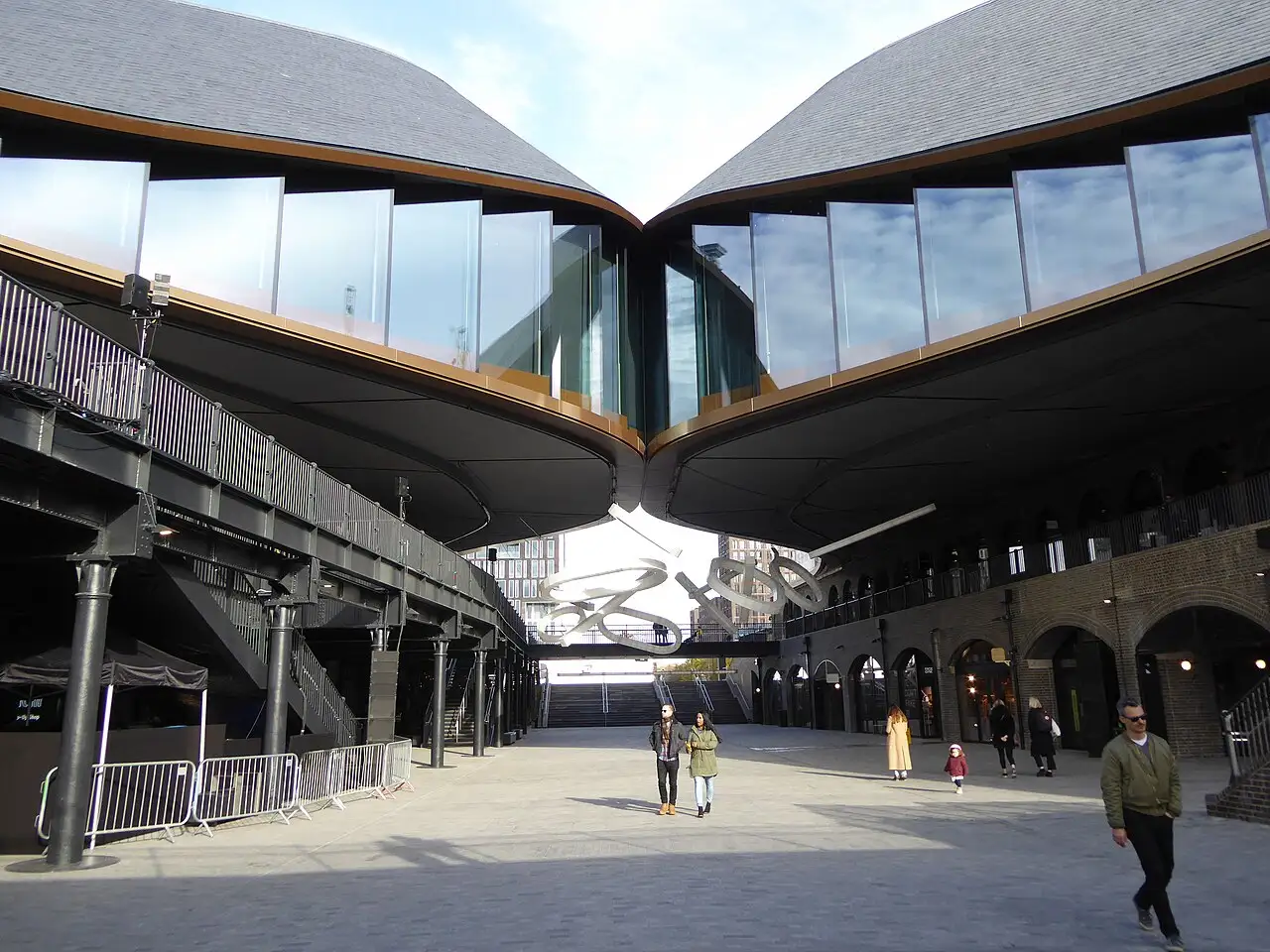 Il cortile di Coal Drops Yard sotto i due tetti in ardesia che si curvano fino a toccarsi, con vetrate, archi in mattoni e passerelle in ghisa