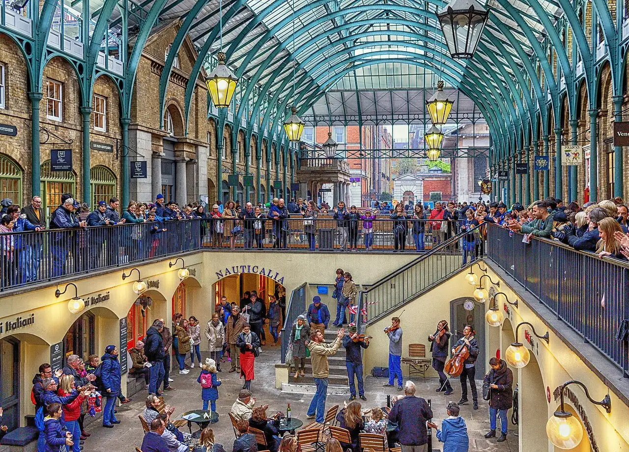 Il cortile ribassato del mercato di Covent Garden sotto la copertura in ferro e vetro, con un quartetto d'archi che suona e il pubblico affacciato alla balaustra