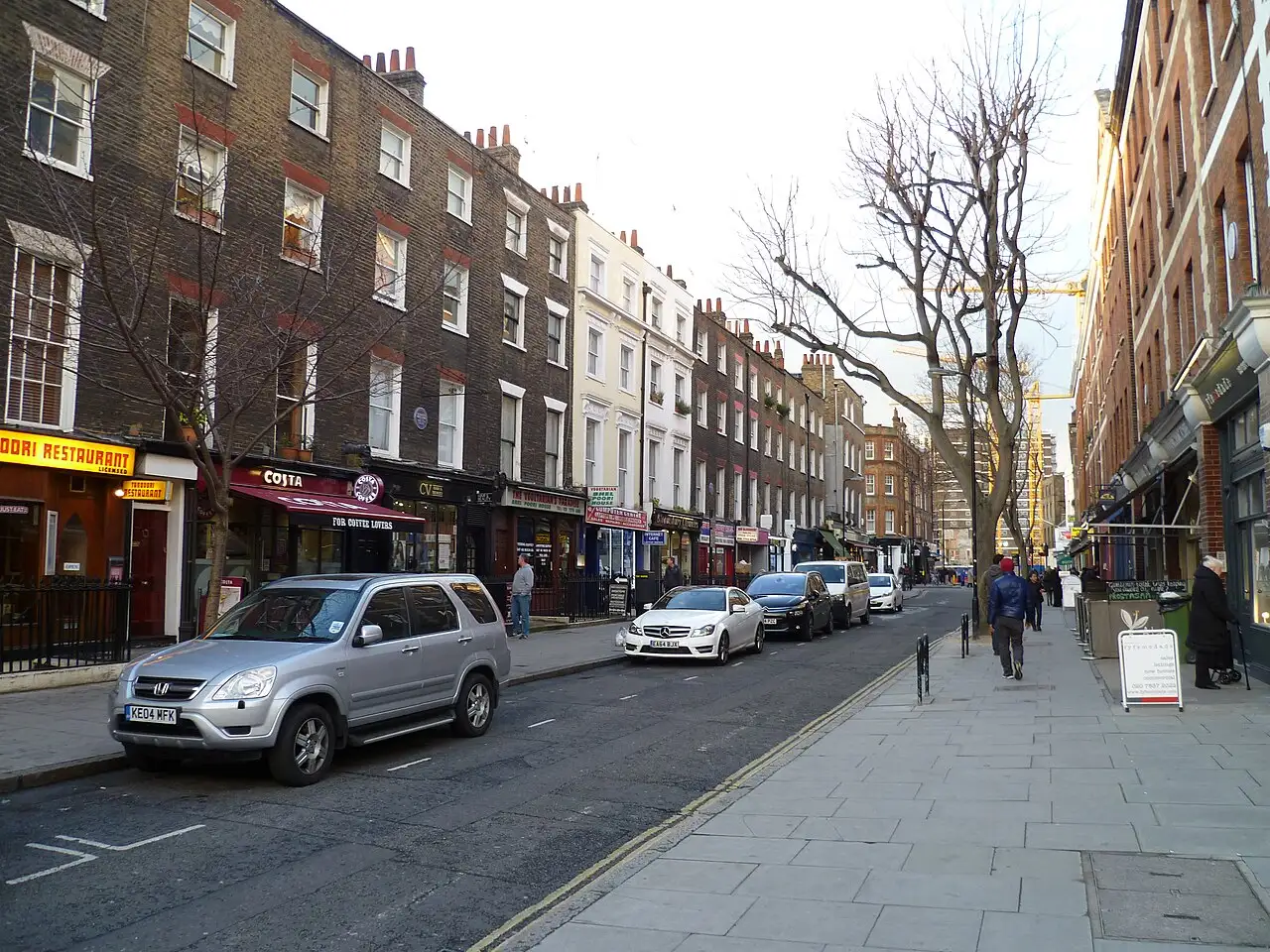 Marchmont Street con le case a schiera georgiane in mattoni scuri, i negozi al piano terra e gli alberi spogli lungo il marciapiede