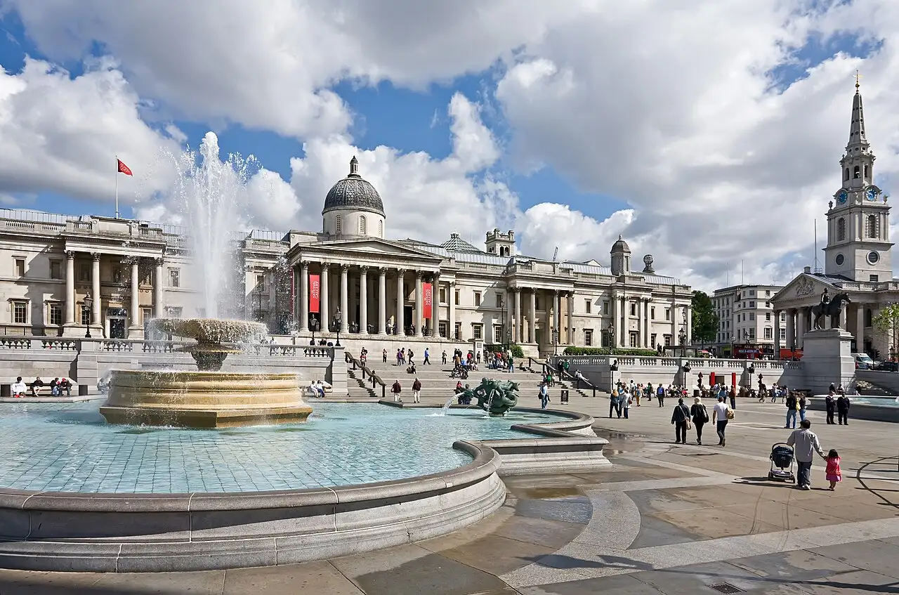 Trafalgar Square in una giornata di sole: una fontana in primo piano, la National Gallery con la cupola sul fondo e il campanile di St Martin-in-the-Fields a destra